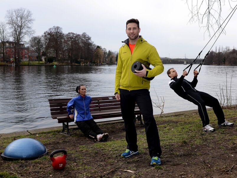 Christian Blisse, Personal Trainer, blickt in die Kamera, zwei Personen trainieren im Hintergrund.