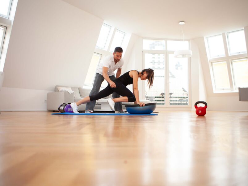 Trainer und Klientin im Wohnzimmer, Klientin trainiert auf Matte.