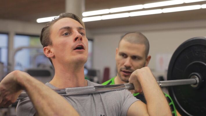 Trainer und Klient beim Hanteltraining, Klient stemmt Hantelstange.